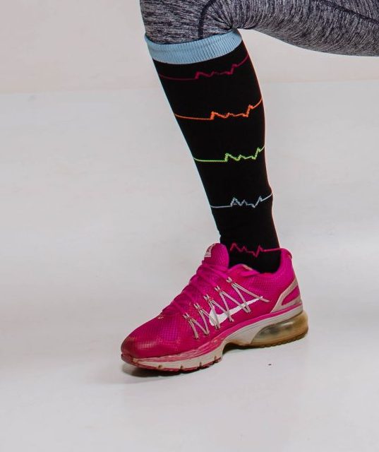 Foto de perna com meia compressiva esportiva preta estampada e tênis rosa