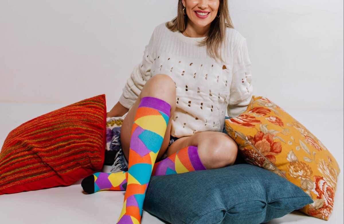 Mulher sentada sobre almofadas, vestindo meias compressivas coloridas