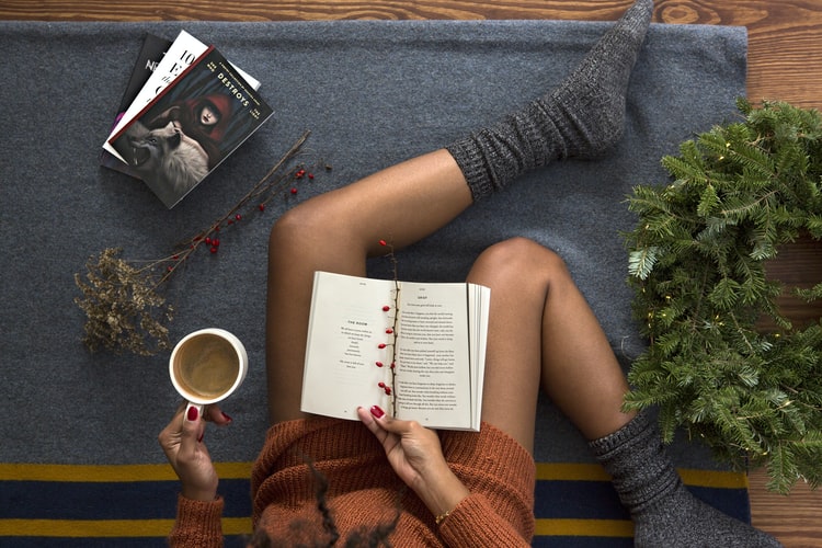 Mulher sentada com pernas à mostra, lendo livro e tomando café